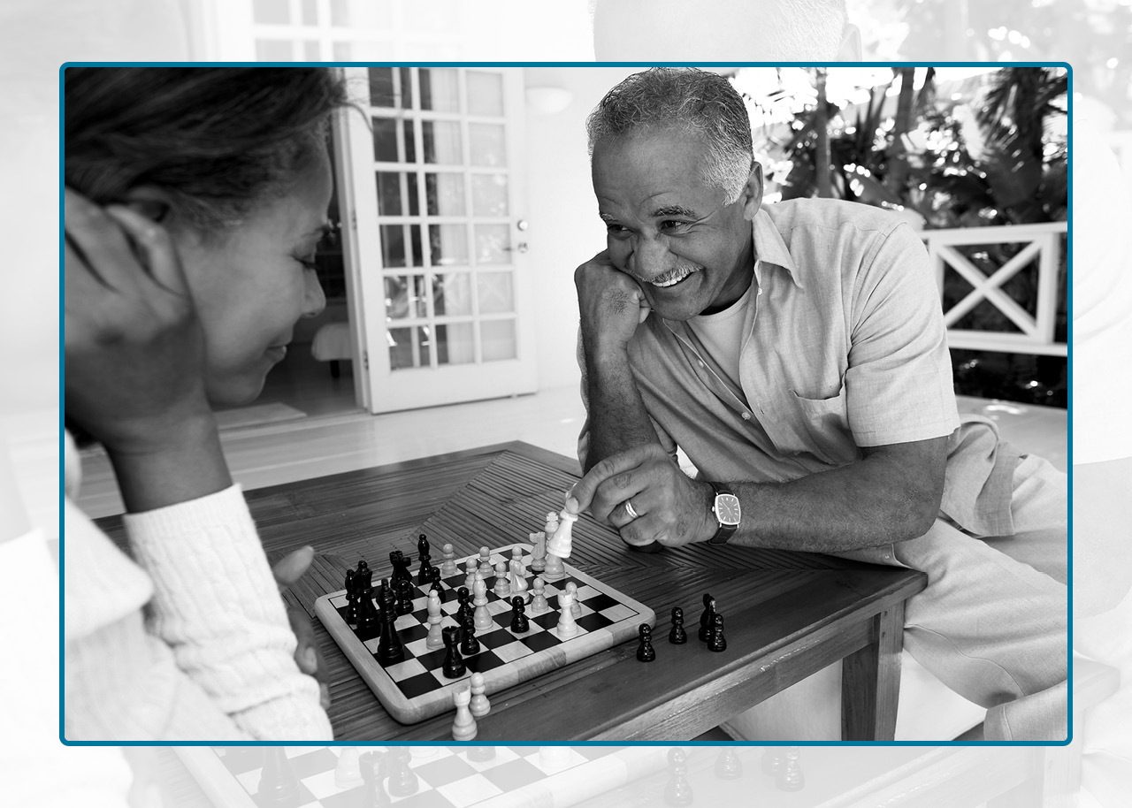 Black and white image of two seniors playing chess on a back deck